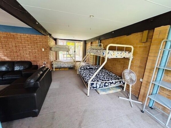 A room with a bunk bed, a black leather sofa, a small table, and a fan.