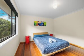 A bedroom with a bed, a nightstand, a red lamp, and a painting on the wall.