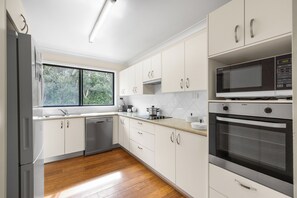 A modern kitchen with white cabinets, stainless steel appliances, and a window providing a view of greenery outside.