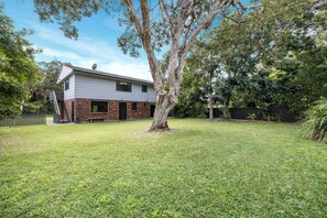 A two-story house with a brick facade and a flat roof, surrounded by a well-maintained lawn and trees.