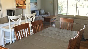 A dining area with a table and chairs, a kitchen area with a microwave, a sofa, and a painting on the wall.