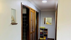 A hallway with wooden flooring, a yellow chair, and a closed door with a mirror.