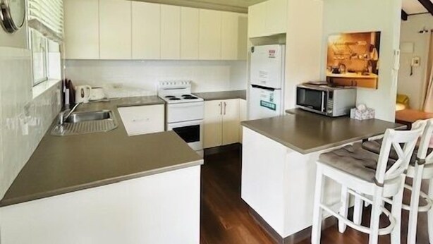 A compact kitchen with white cabinets, a built-in stove, a microwave, and a small island with seating.