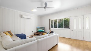 A modern living room with a white sofa, a flat-screen TV, and a ceiling fan. - Beach Break - 22 Bay St Hat Head (Hat Head)