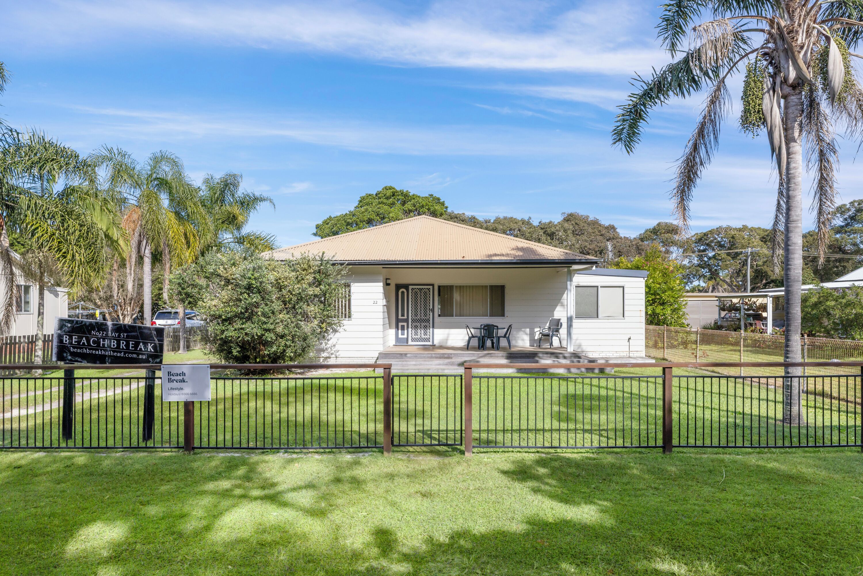 A single-story house with a beige roof, a front porch with a table and chairs, and a fenced yard.