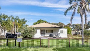 A single-story house with a beige roof, a front porch with a table and chairs, and a fenced yard. - Beach Break - 22 Bay St Hat Head (Hat Head)