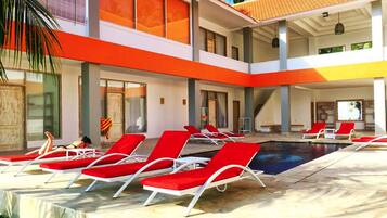 A pool area with red lounge chairs, a clear pool, and a modern building with orange and white colors.