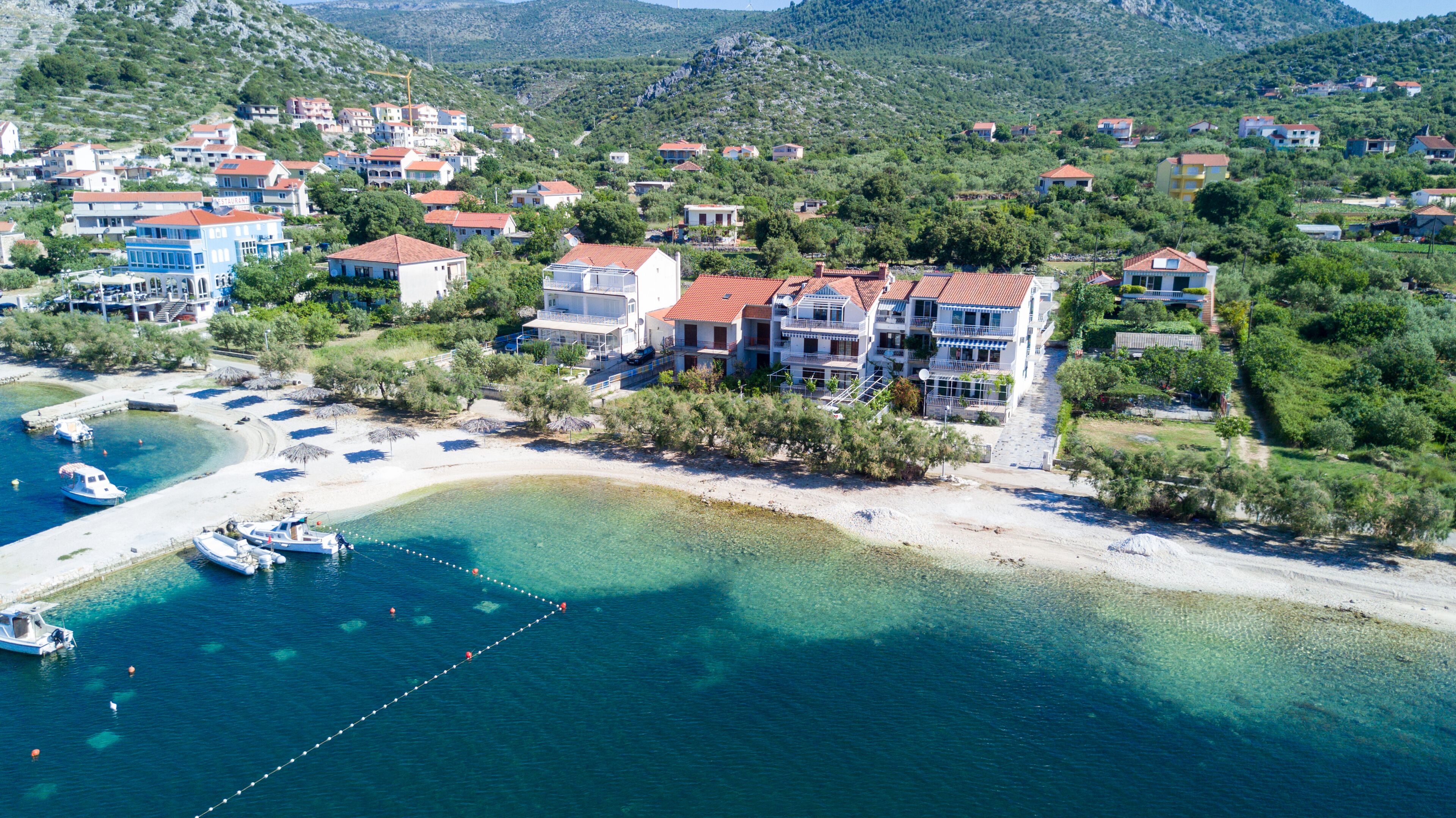 Una vista aerea di una cittadina costiera con edifici, una spiaggia e barche.