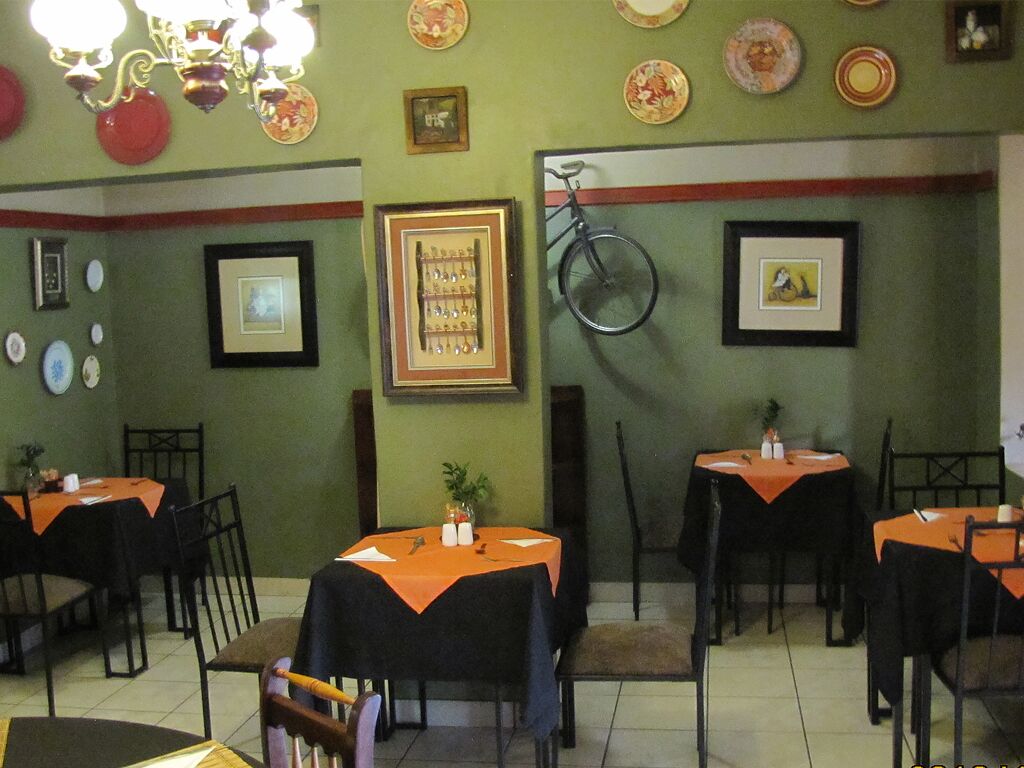 A restaurant interior with tables covered in orange tablecloths, framed pictures on the walls, and a bicycle hanging on the wall.