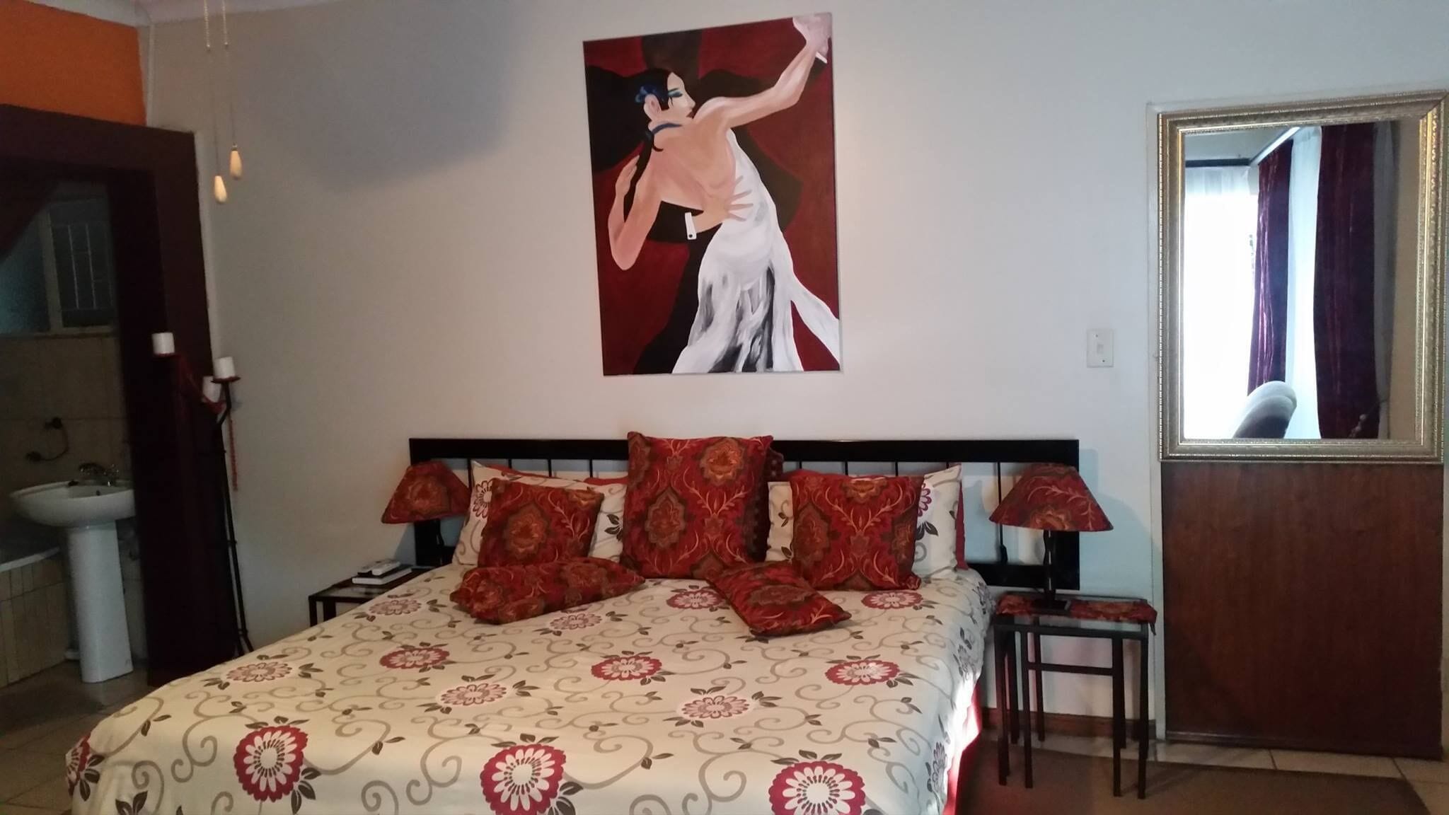 Un dormitorio con cama, mesita de noche, lámpara, espejo y un cuadro en la pared.