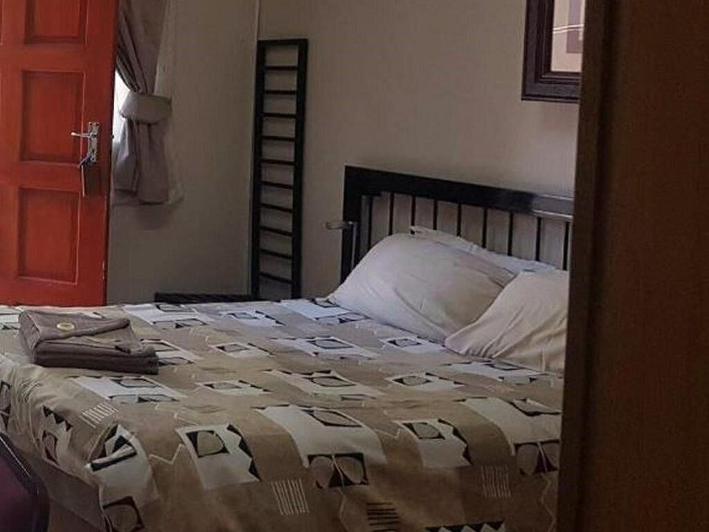Un dormitorio con una cama, una puerta roja y una escalera apoyada en la pared.
