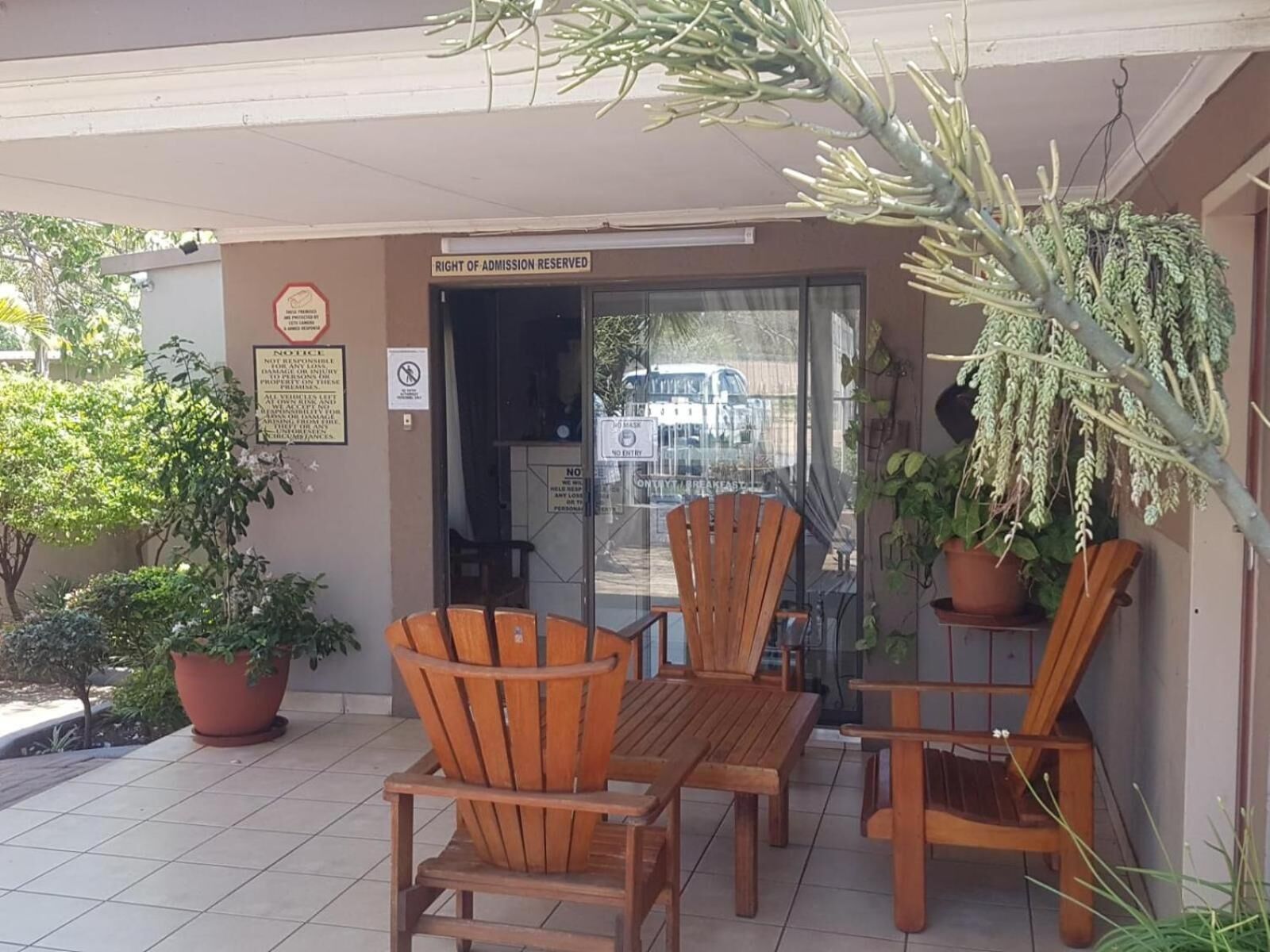 Un espace extérieur aménagé avec des chaises et des tables en bois, un panneau indiquant que l’établissement se réserve le droit d’admission, et des plantes en pot.