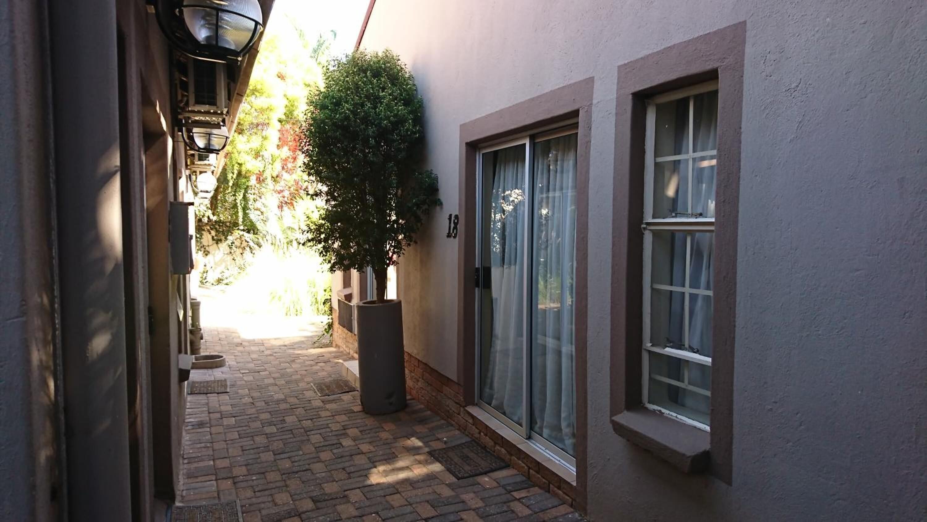 Une ruelle étroite, avec un arbre en pot, une porte portant le numéro « 18 » et une fenêtre avec des rideaux.