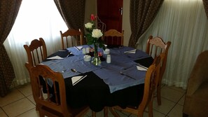 Una mesa redonda de comedor con mantel azul, rodeada de sillas de madera. Un jarrón con rosas blancas y rosadas está colocado en el centro.