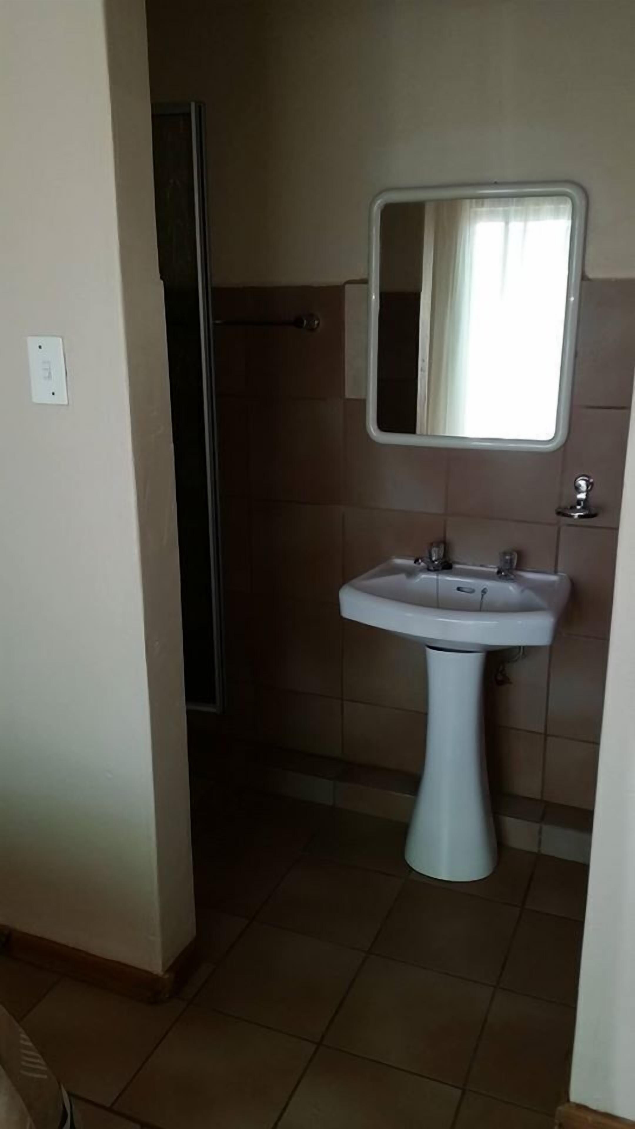 Une salle de bain avec un lavabo sur colonne, un miroir au-dessus, et un espace douche visible à travers une porte.