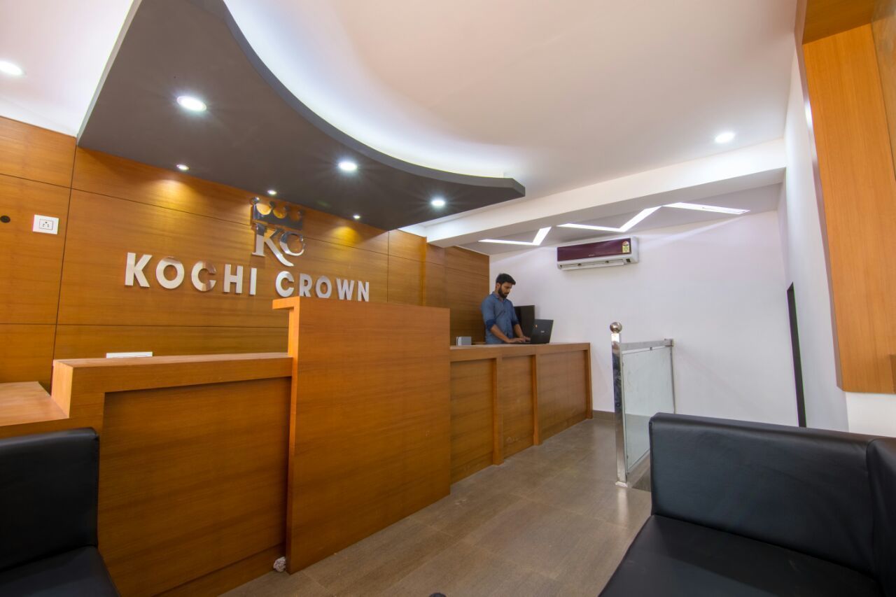 A reception area with a wooden reception desk, a person behind it, and a seating area with black chairs.