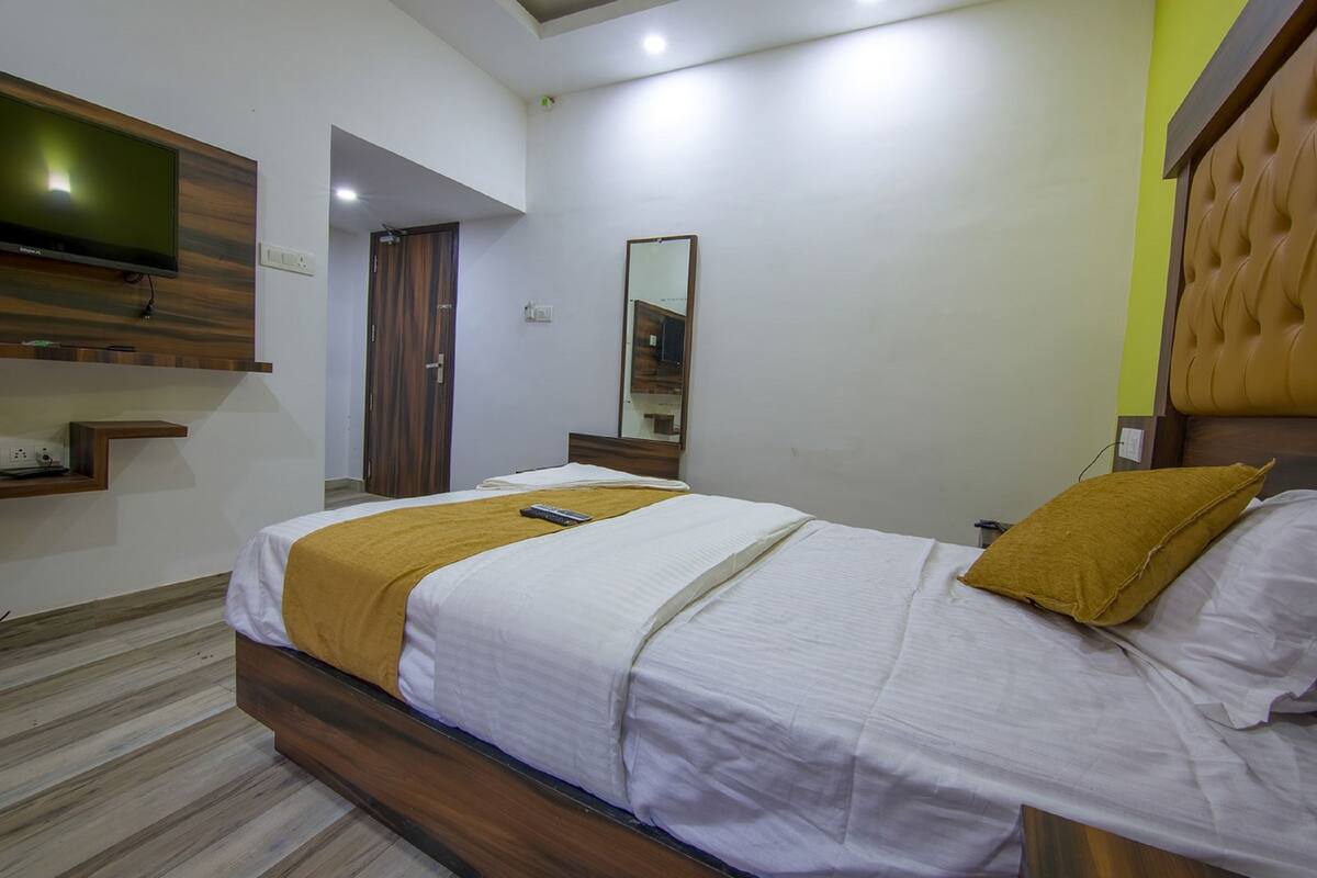A hotel room with a bed, a television mounted on the wall, a mirror, and a wooden headboard.