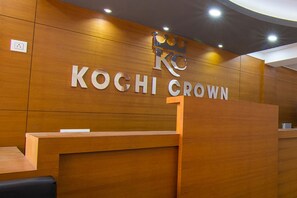 A reception desk with a wooden finish and a sign that reads "KOGHI CROWN". - Hotel Kochi Crown (Kanayannur)