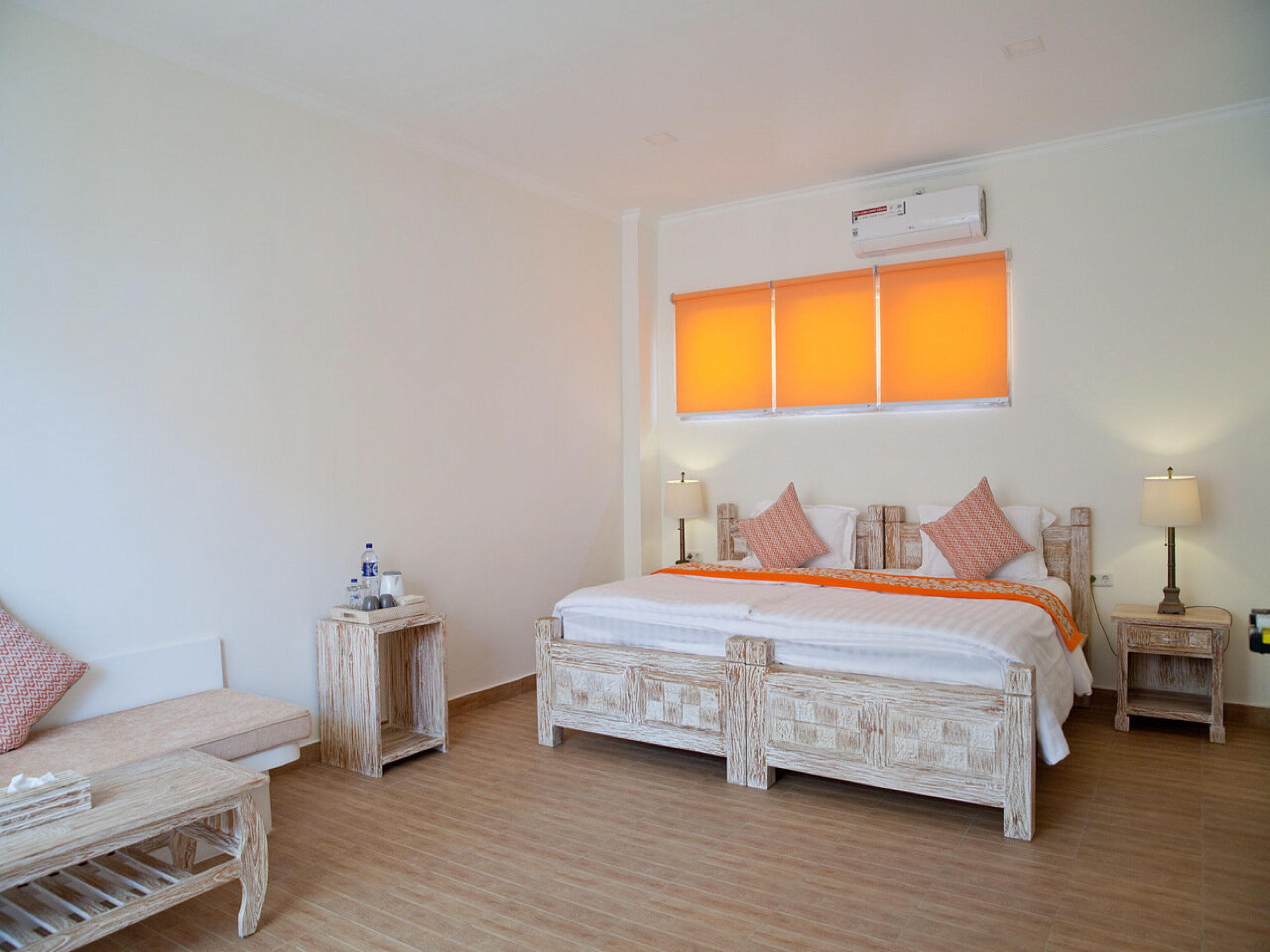 A bedroom with a large bed, two bedside tables, a nightstand, a chair, and a window with blinds.