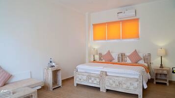 A bedroom with a large bed, two bedside tables, a nightstand, a chair, and a window with blinds.