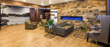 A modern lobby with a stone wall, a fireplace, leather sofas, and a large mural of a lake.