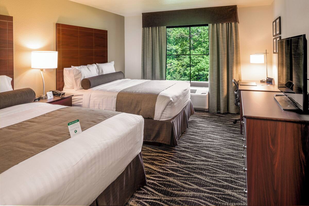 A hotel room with two beds, a desk with a chair, a TV, and a window with curtains.