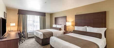 Una habitación de hotel con dos camas, un escritorio, un televisor y una ventana con cortinas.