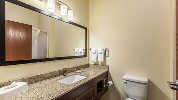 A bathroom with a granite countertop sink, a large mirror, a towel rack, and a toilet.