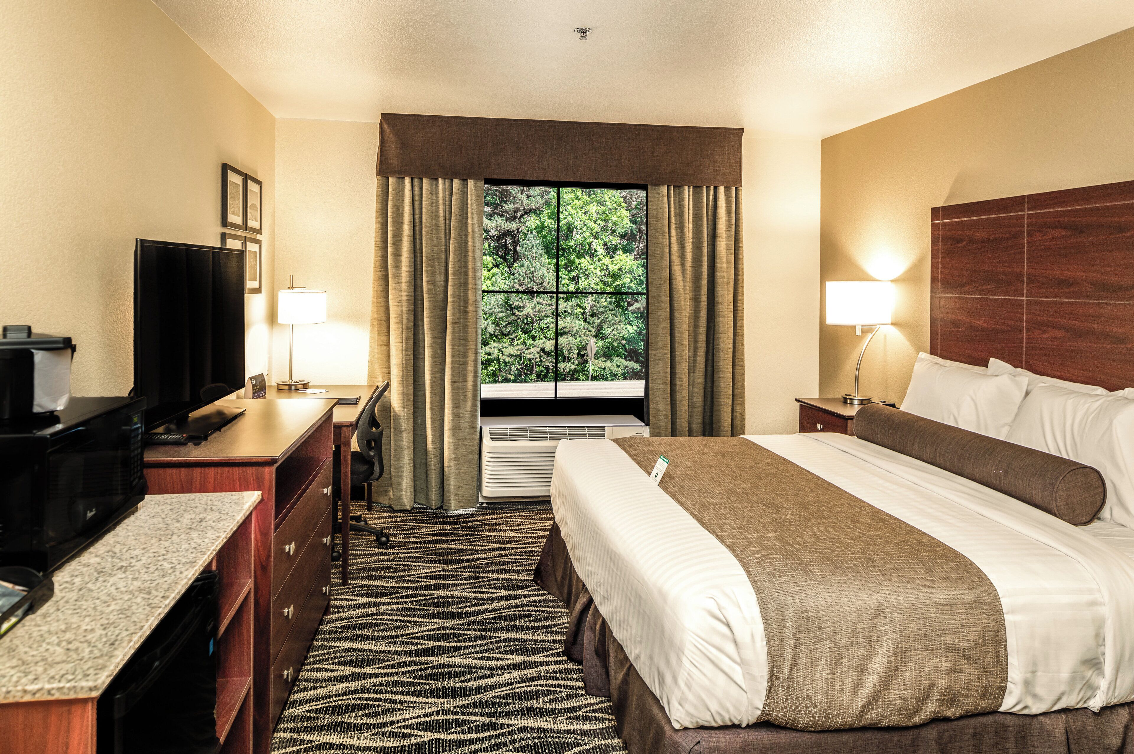 A hotel room with a bed, desk, television, and a window with curtains.
