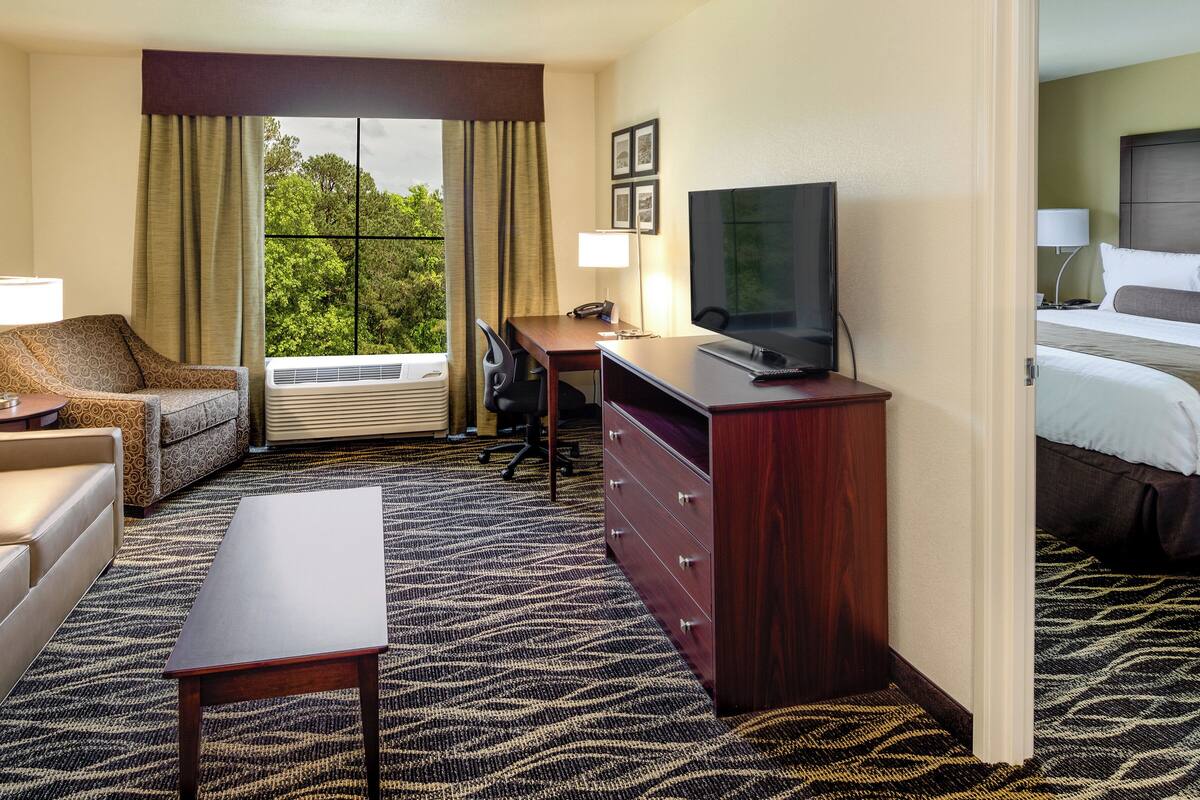 A hotel room with a sofa, a desk, a television, a dresser, and a window with curtains.