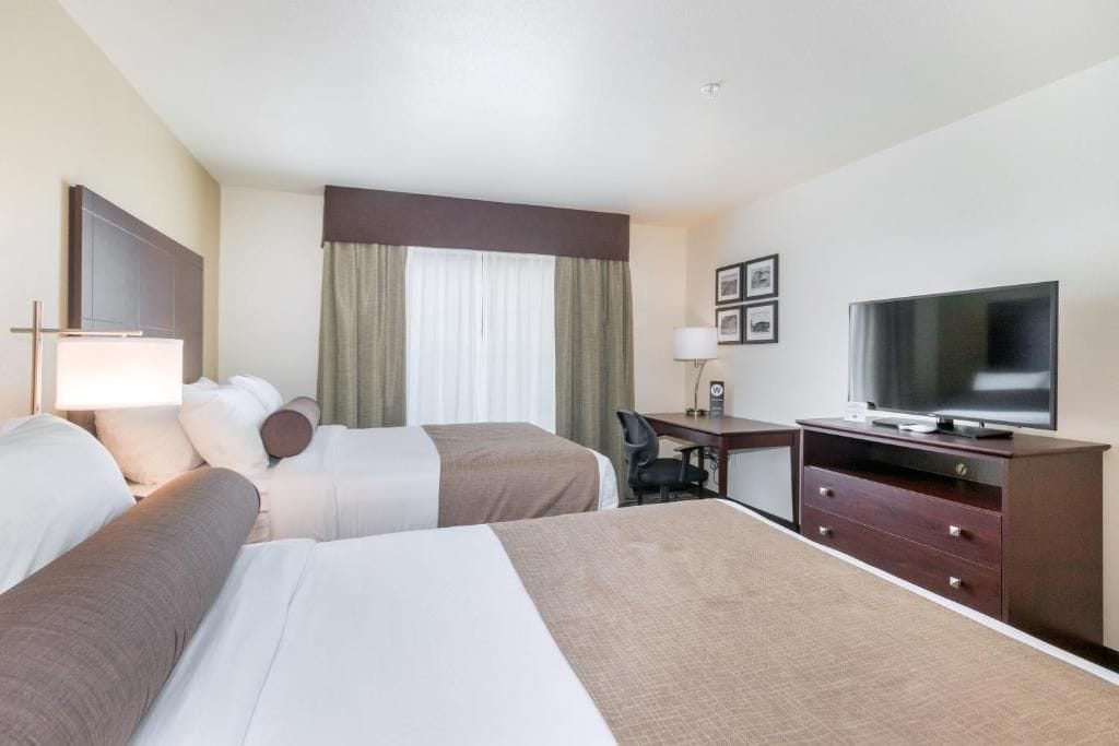 A hotel room with two beds, a desk, a television, and a chair.