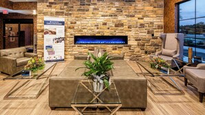 A modern lobby with a stone wall, a fireplace, leather sofas, and a glass coffee table. - Cobblestone Inn & Suites - Fairfield Bay (Fairfield Bay)