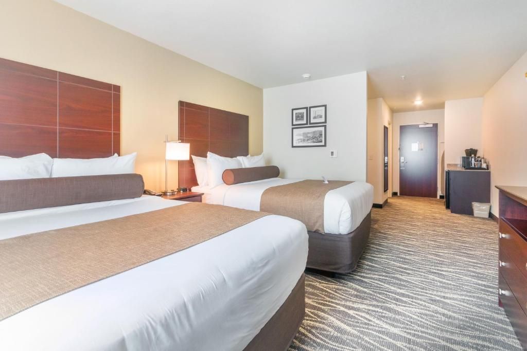A hotel room with two beds, a desk, and a lamp.
