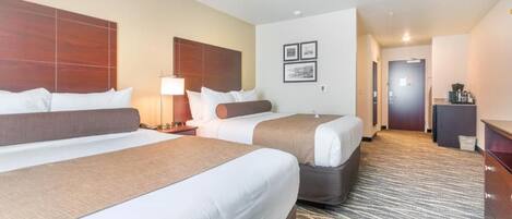 A hotel room with two beds, a desk, and a lamp.