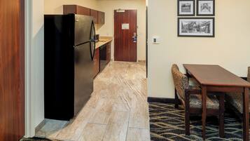 A compact kitchen with a refrigerator, wooden cabinets, and a marble-tiled floor. There is a dining area with a table and patterned bench.