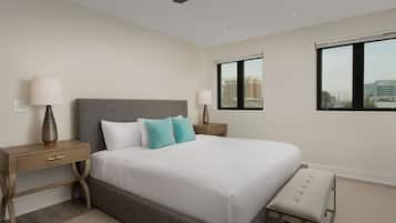 Una habitación de hotel moderna con una cama grande, dos mesitas de noche, un ventilador de techo y vistas a edificios a través de la ventana.