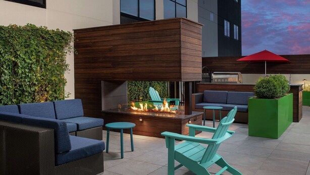 An outdoor seating area with a fire feature, a sofa, chairs, and a grill. - Home2 Suites by Hilton Nashville Downtown Convention Center (Nashville)