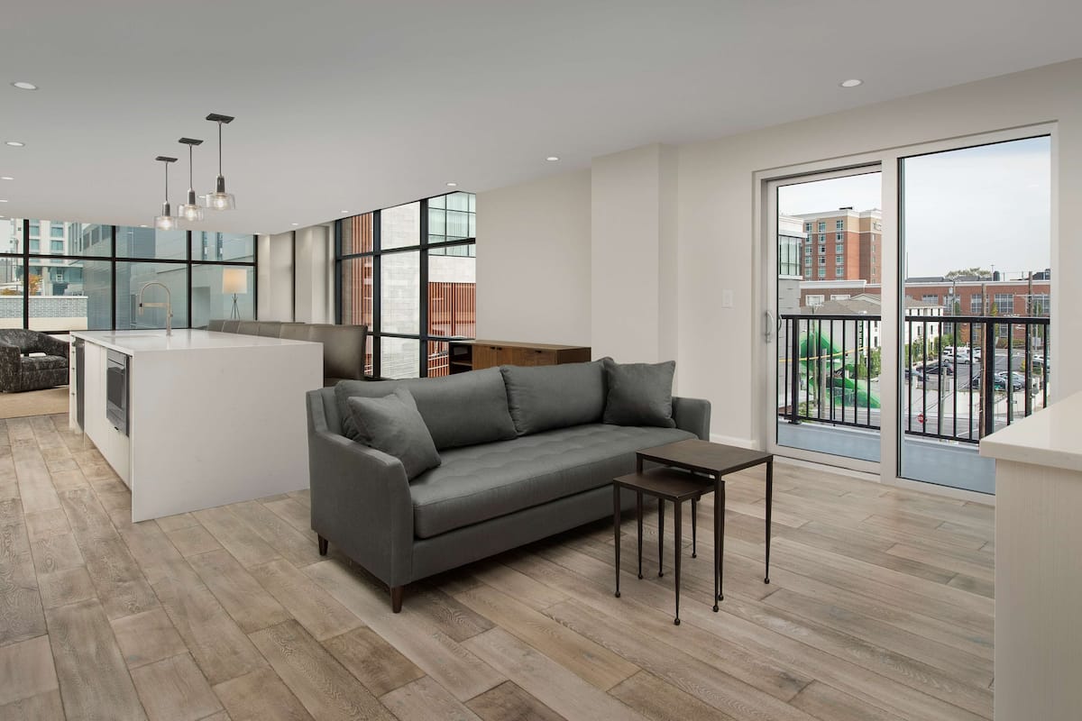 A modern apartment with a grey sofa, a small table, and a kitchen area.
