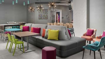 Un espace de détente moderne avec un canapé d’angle gris, des fauteuils colorés, une table en bois et un pouf rouge.
