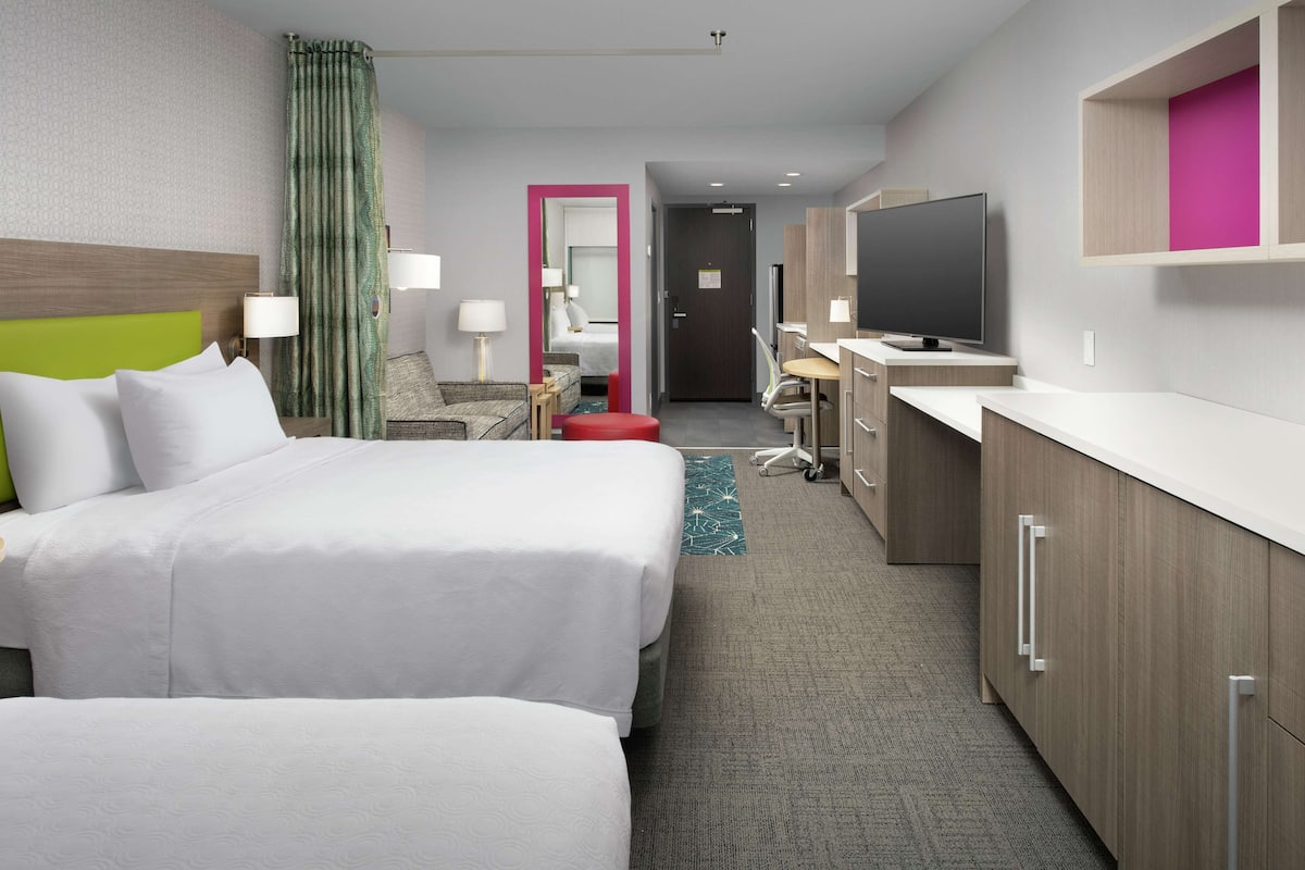 A hotel room with two beds, a desk, a TV, and a bathroom.