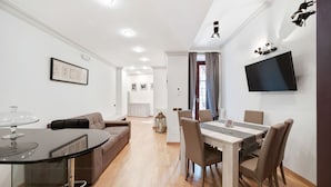 A modern living room with a dining area, a TV mounted on the wall, and a cozy seating arrangement. - Peroni Apartment (Rome)