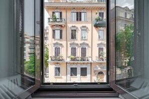 A view through a window of a building with multiple balconies, ornate architectural details, and a clear sky. - Peroni Apartment (Rome)