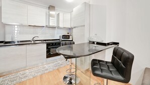 A modern kitchen with white cabinetry, a built-in oven, a microwave, and a glass-top dining table with a black leather chair. - Peroni Apartment (Rome)