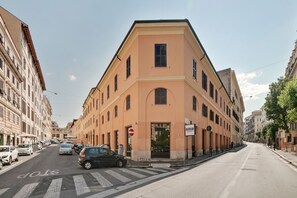 A street view of a building with a corner entrance, parked cars, and a pedestrian crossing. - Peroni Apartment (Rome)