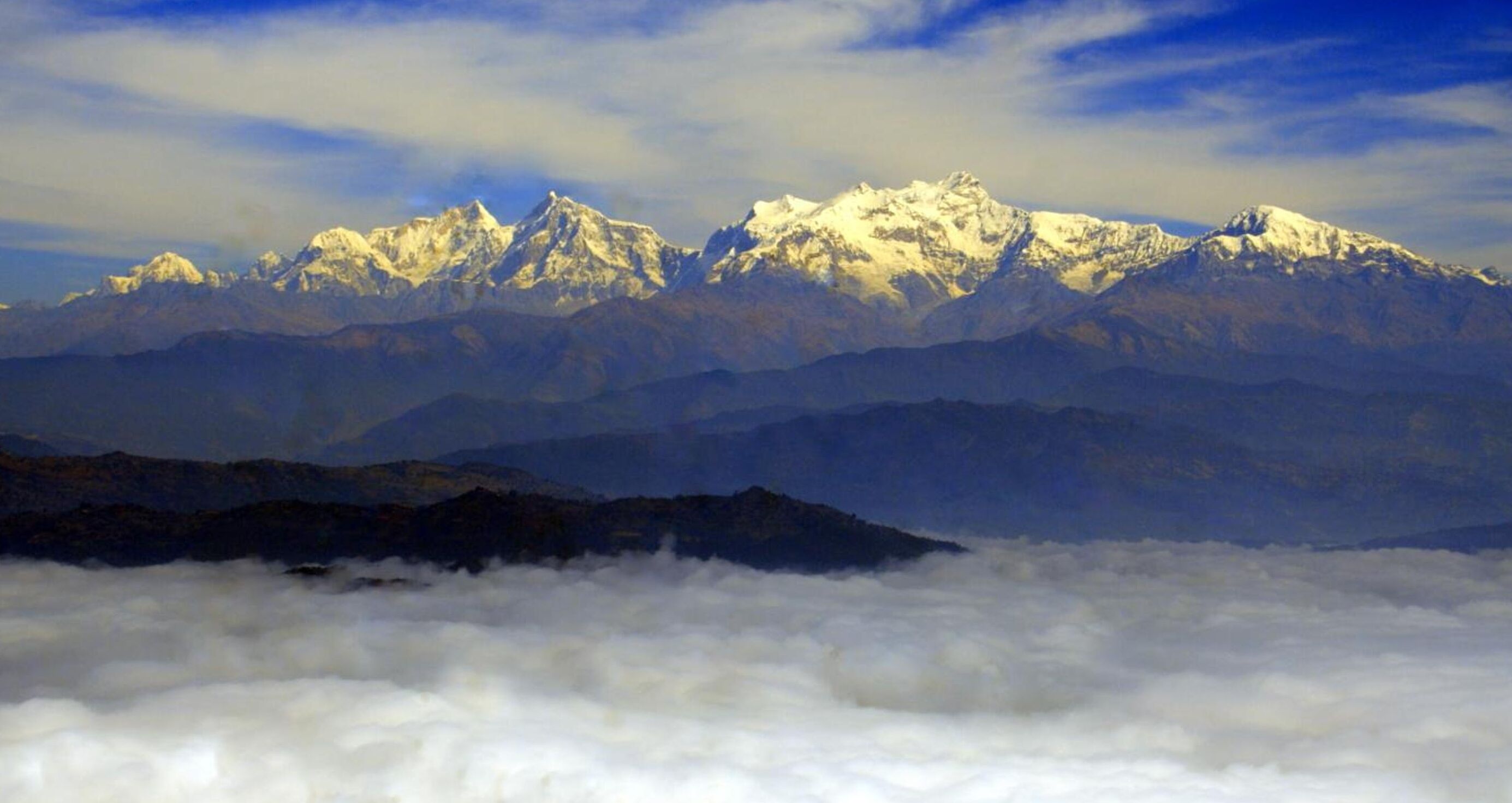 A mountain range with snow-capped peaks and a layer of clouds below.
