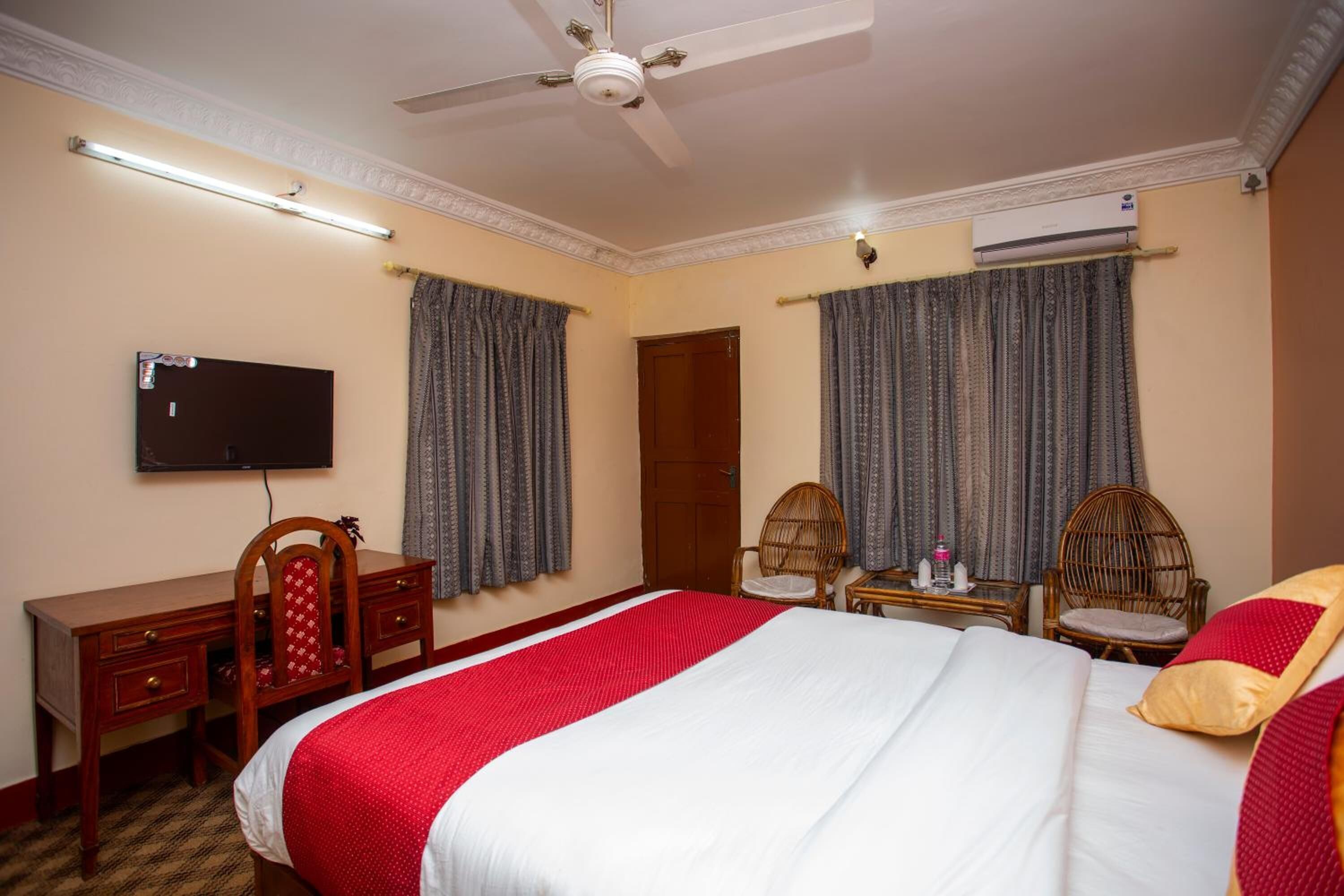 A hotel room with a bed, a desk, two chairs, a television, and an air conditioning unit.