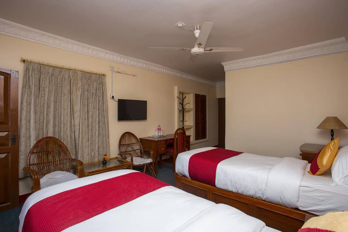 A hotel room with two beds, a desk, a chair, a television, and a ceiling fan.