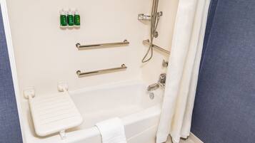A bathroom with a bathtub, grab bars, a showerhead, and toiletries on the wall.