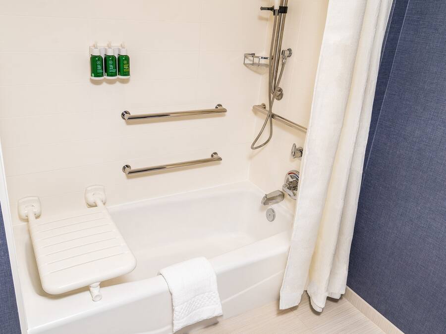 A bathroom with a bathtub, grab bars, a showerhead, and toiletries on the wall.