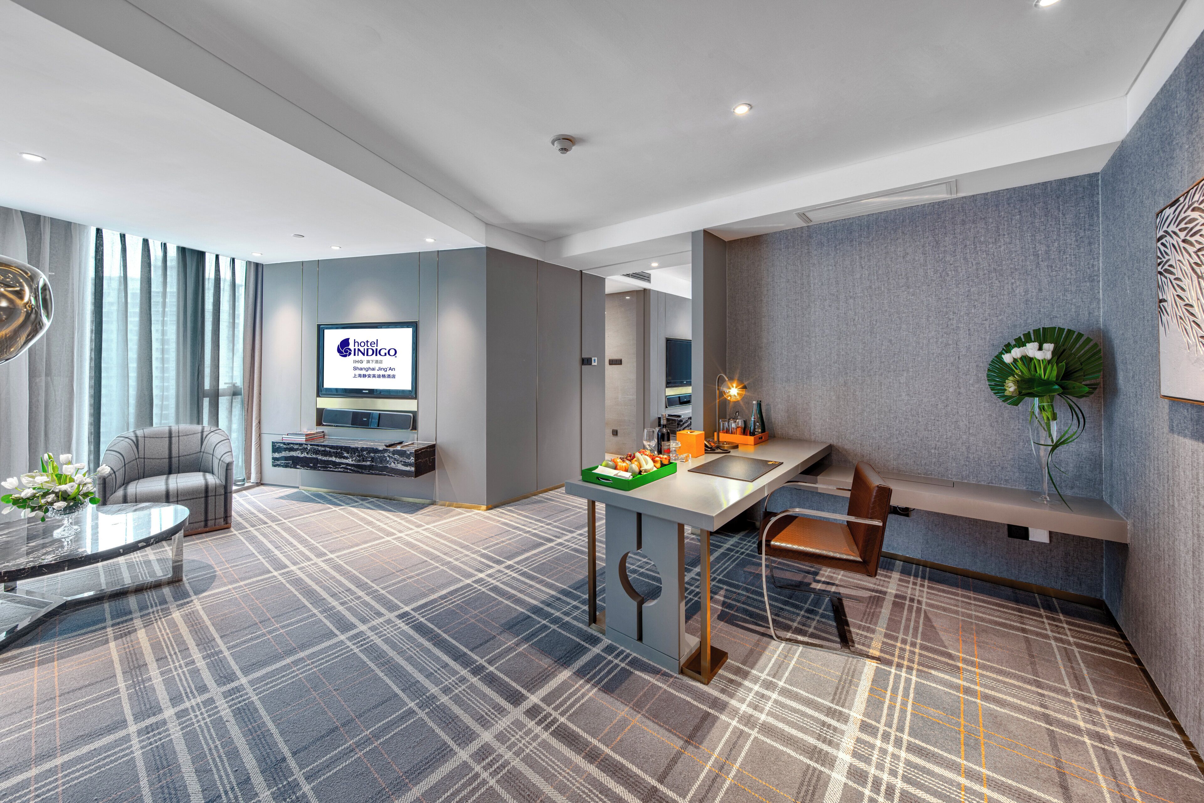 Habitación de hotel moderna con sofá, mesa de comedor, pequeña cocina y televisión de pantalla plana.
